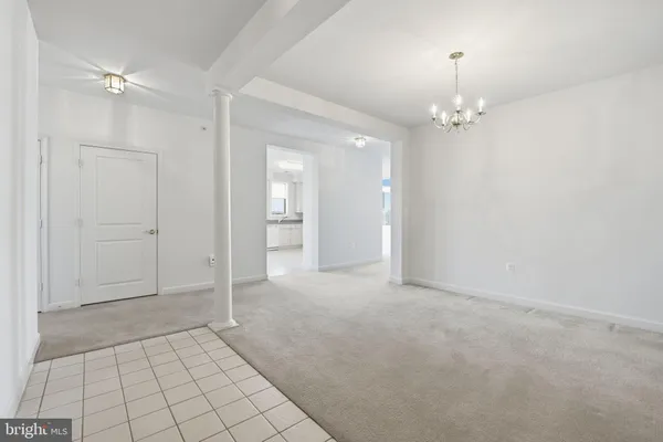 an empty room with chandelier fan and kitchen view
