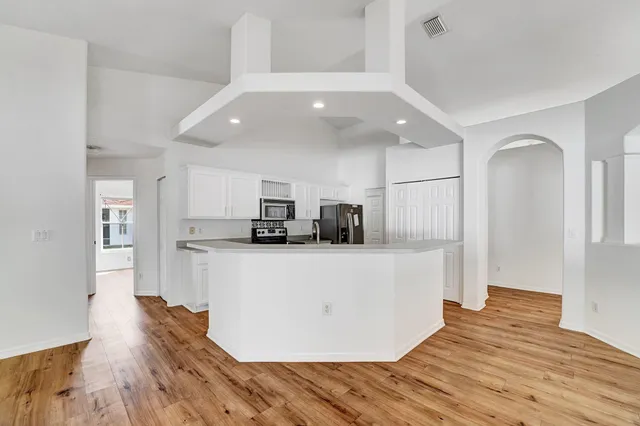 a living room with stainless steel appliances kitchen island granite countertop a refrigerator a stove and a wooden floor