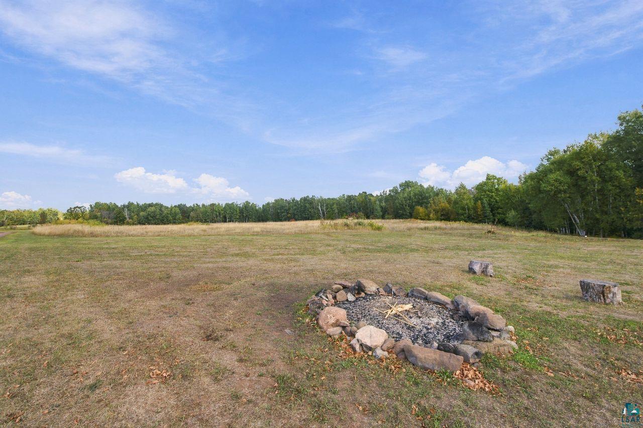 65889 Old County Road Marengo, WI 54855 - Photo 34 of 44 Expansive open field with a natural tree line, featuring a built-in stone fire pit and natural log seating