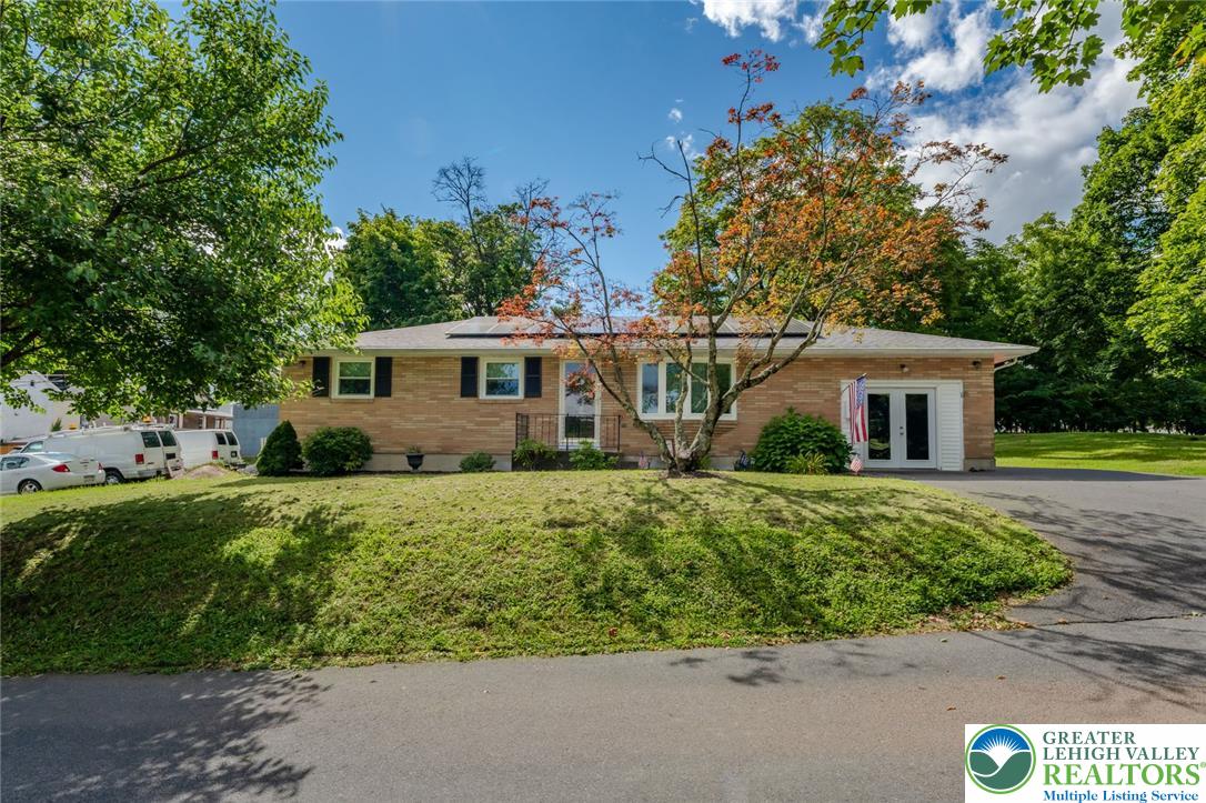 402 Maple Street Roseto, PA 18013 - Photo 3 of 39 Mature trees frame a classic brick ranch exterior featuring a paved driveway and elevated lawn.