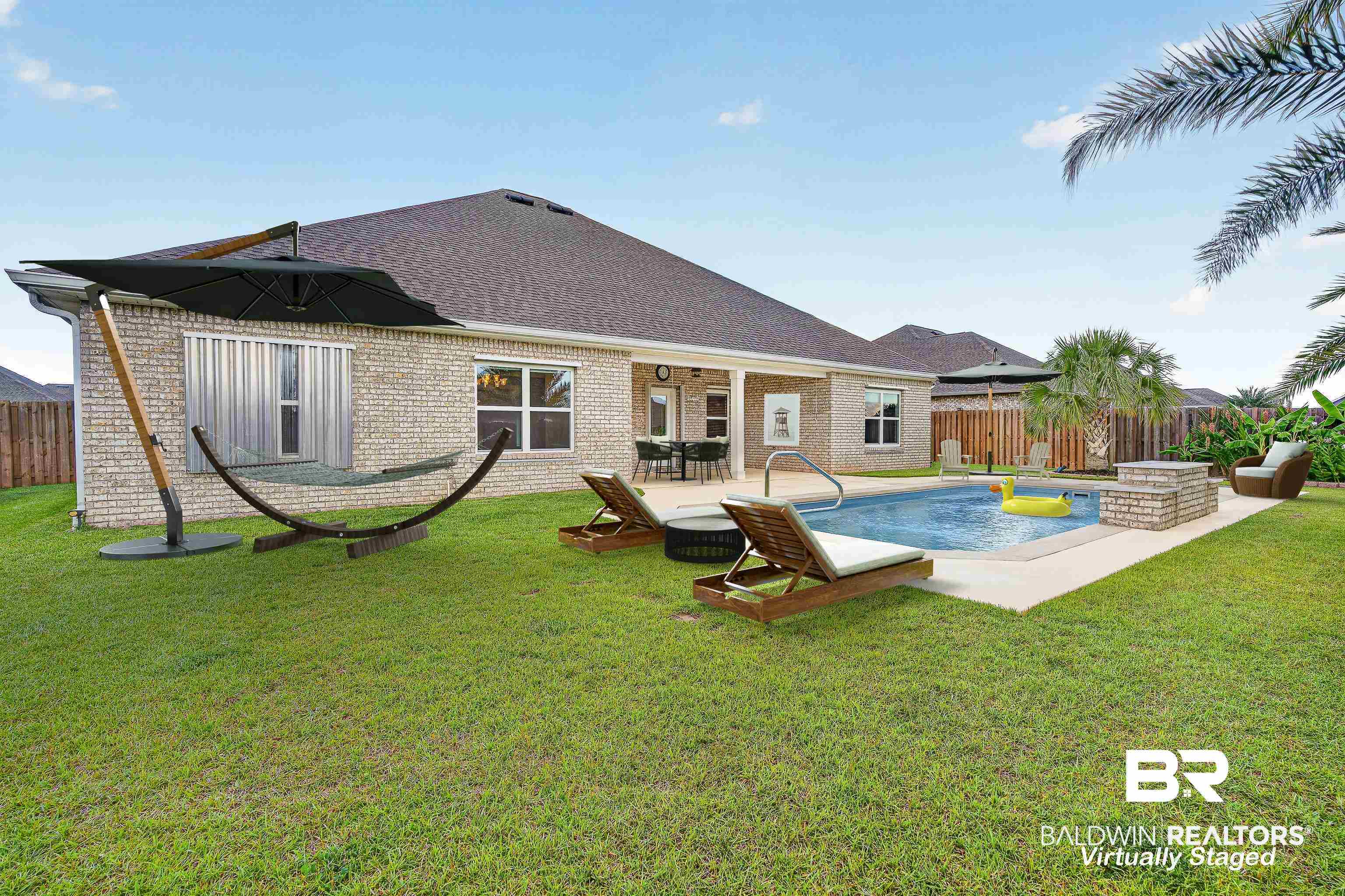 1724 Partridge Street Foley, AL 36535 - Photo 52 of 62 Expansive green lawn featuring an in-ground swimming pool with surrounding concrete decking, a brick and stone outdoor fireplace, and mature palm trees