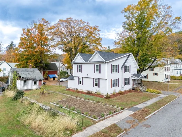 a view of a white house next to a yard with big trees