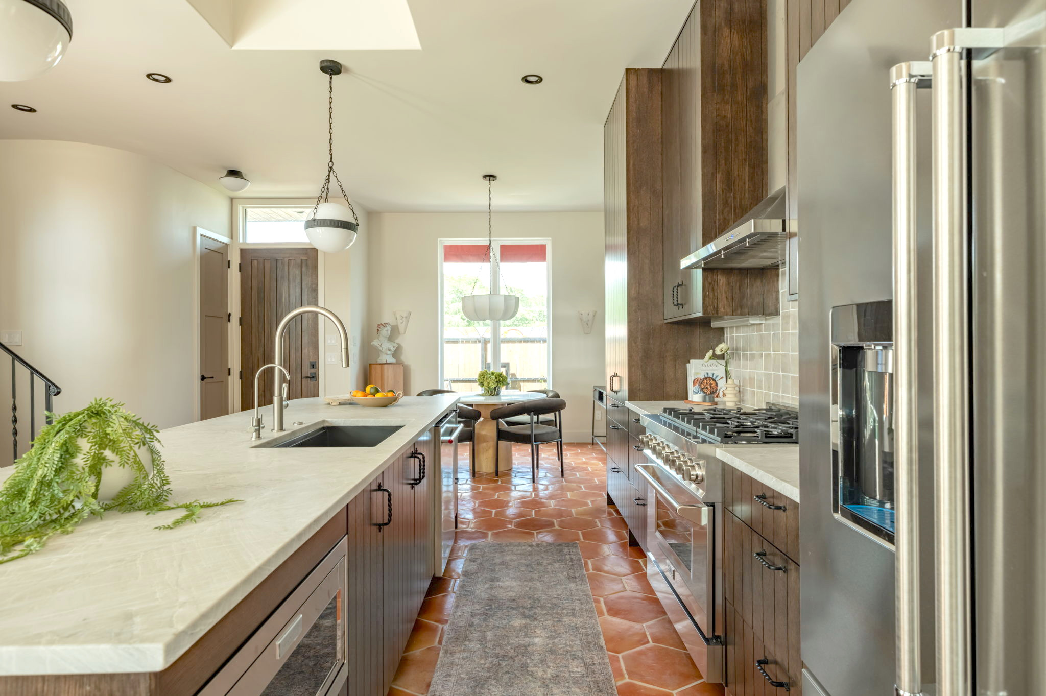 4713 Bolm Road Austin, TX 78702 - Photo 10 of 40 Gourmet kitchen featuring a large central island with an undermount sink, stainless steel appliances, wood-finish cabinetry, and terracotta hexagon tile flooring