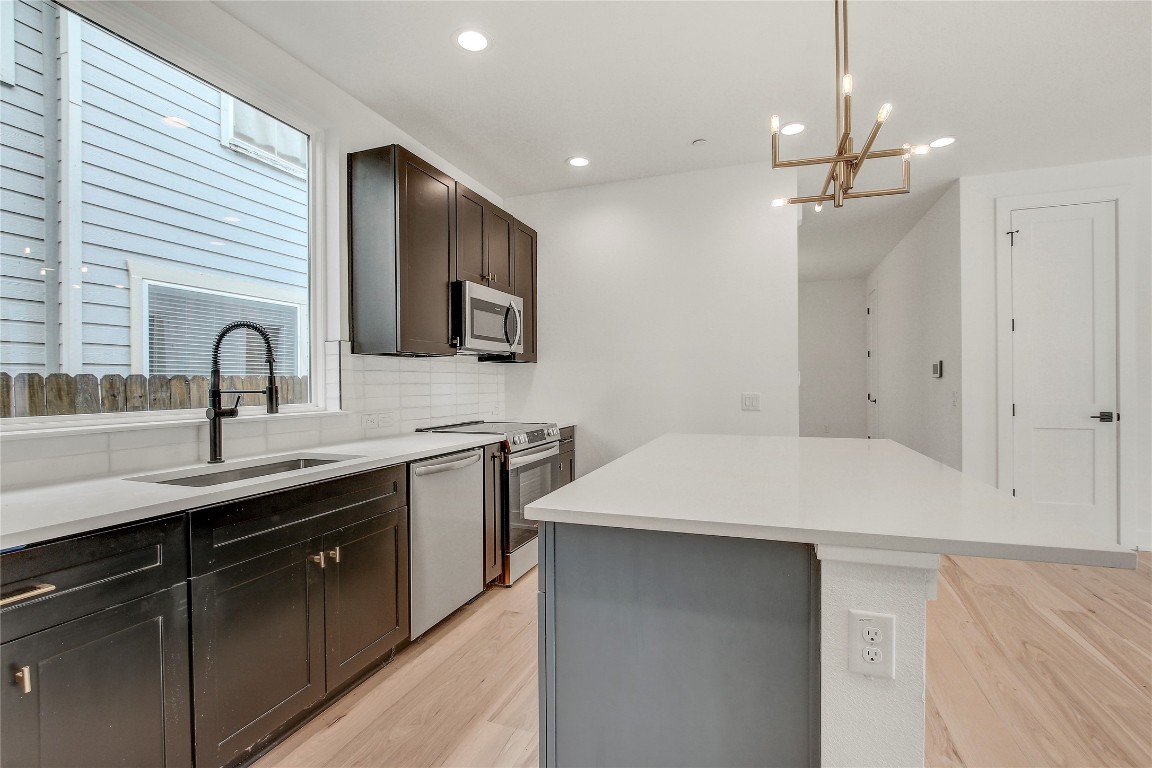 4127 East 12th Street, Unit 2 Austin, TX 78721 - Photo 16 of 28 Kitchen featuring stainless steel appliances, a sink, a kitchen island, light wood finished floors, and backsplash