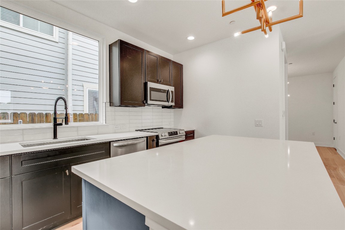 4127 East 12th Street, Unit 2 Austin, TX 78721 - Photo 17 of 28 Kitchen featuring appliances with stainless steel finishes, a sink, light wood-style flooring, dark brown cabinetry, and light countertops