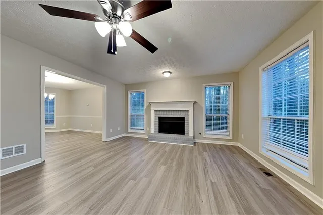 a view of an empty room with wooden floor fireplace and a window