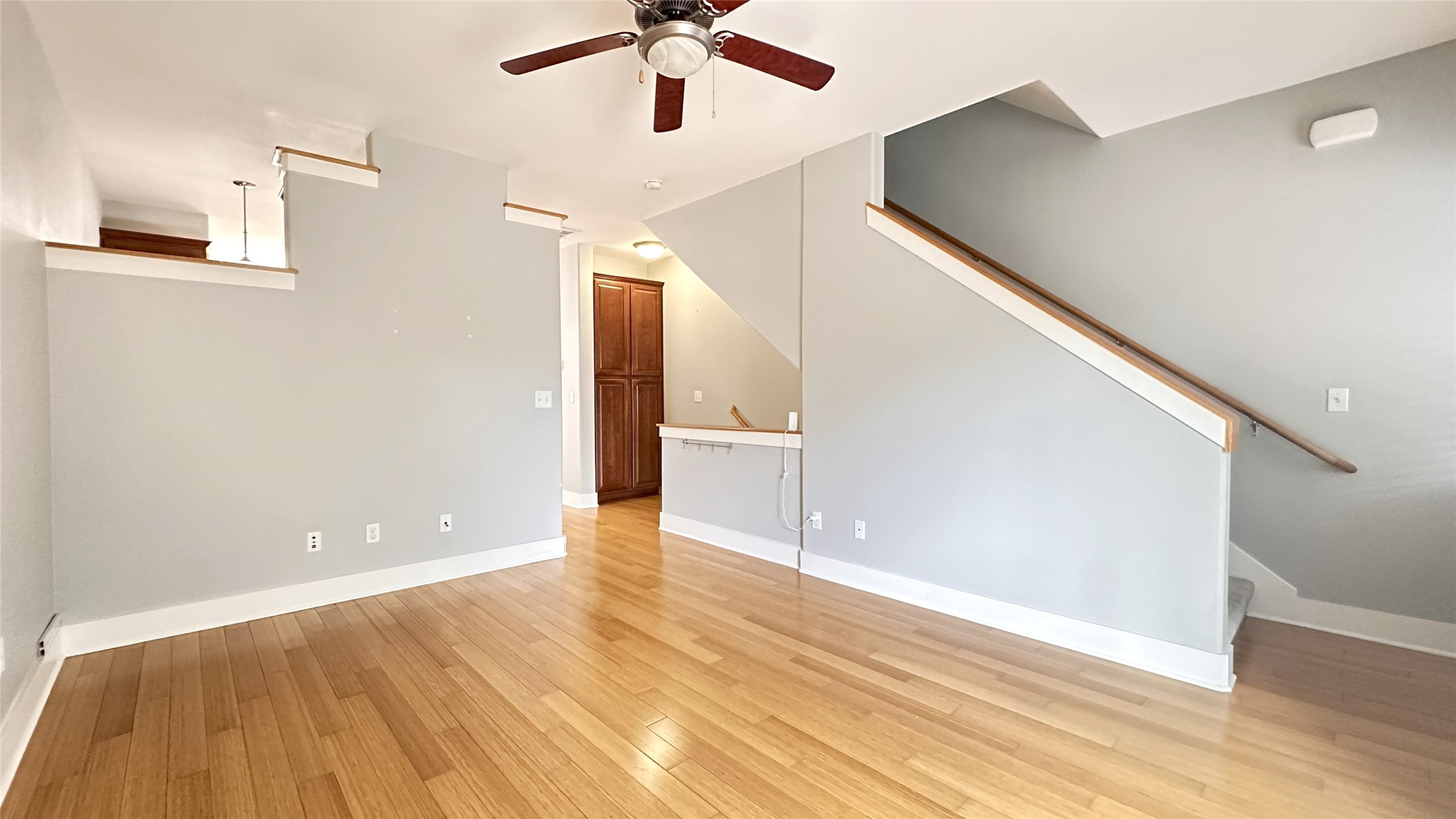 Unfurnished living room featuring light wood-type flooring, a ceiling fan, and stairs