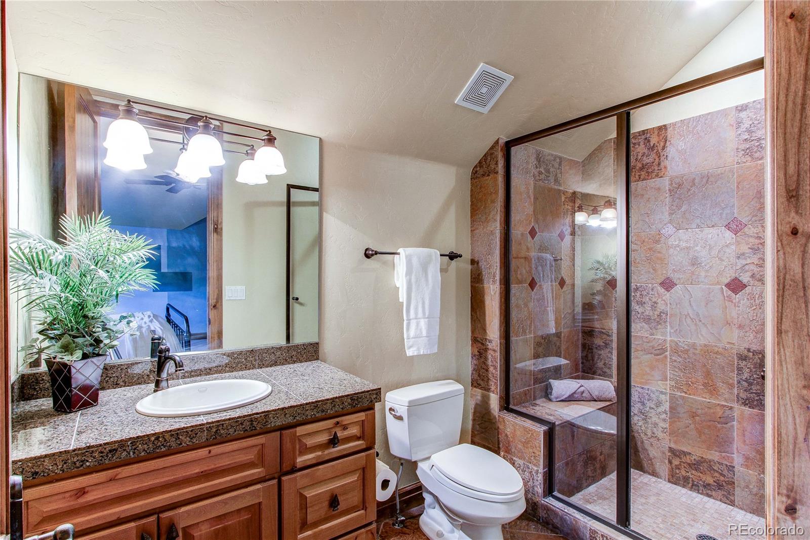 5764 Amber Ridge Drive Castle Pines, CO 80108 - Photo 32 of 50 a bathroom with a granite countertop sink toilet a mirror a glass door and shower