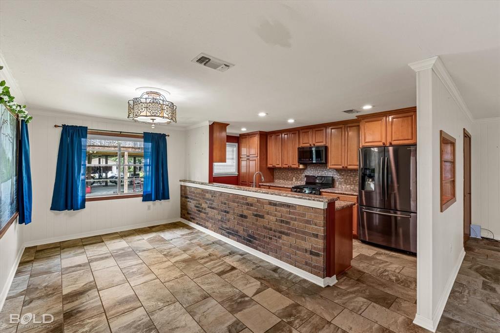 225 Marie Road Ringgold, LA 71068 - Photo 24 of 40 Kitchen and dining area featuring wood-finish cabinetry, stainless steel appliances, brick veneer accent wall, patterned tile flooring, and a decorative ceiling fixture