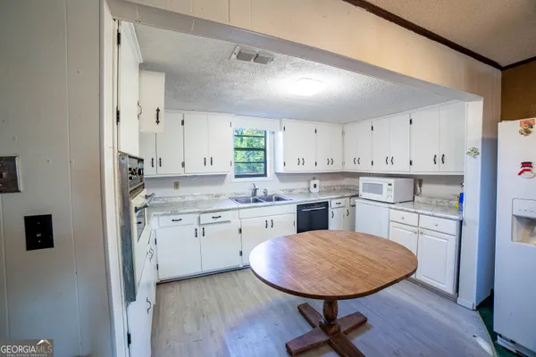 a kitchen with a stove a sink dishwasher a refrigerator with white cabinets and wooden floor