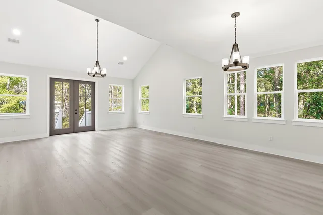 an empty room with wooden floor chandelier and windows