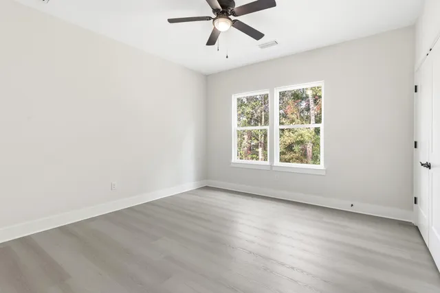 an empty room with wooden floor fan and windows