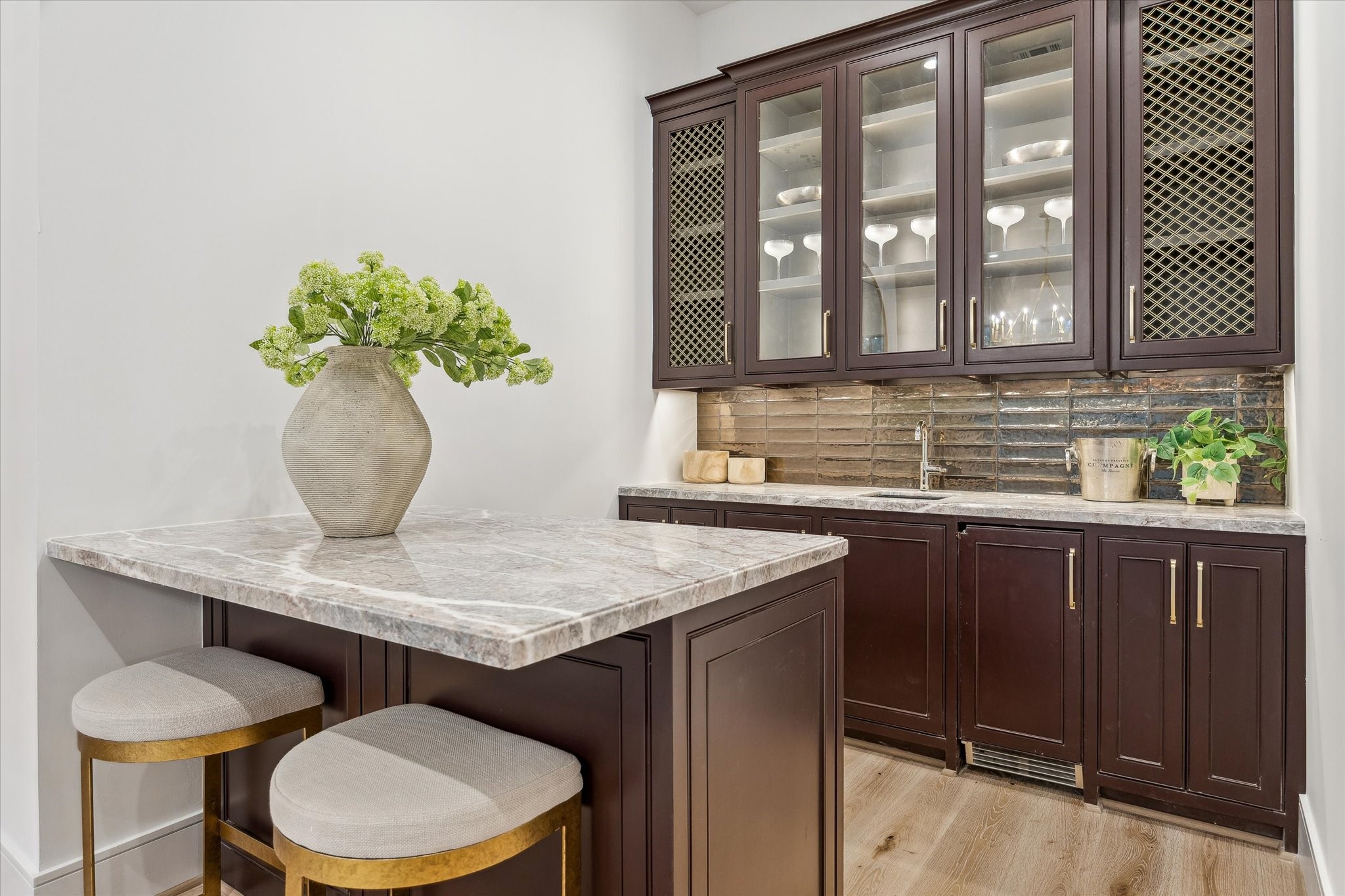 1210 West Drew Street Houston, TX 77006 - Photo 21 of 35 The wet bar off the living room. Quartzite countertops contrast with the dark cabinetry, and brass grills and glass cabinet fronts ensure an elevated feel. Look at those gorgeous metalic coated porcelain tiles in the backsplash! A clear ice maker and beverage coole come built in.