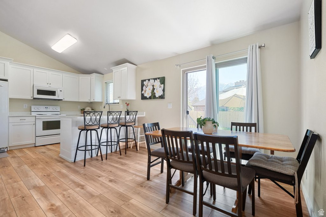 865 South 325 West Orem, UT 84058 - Photo 14 of 38 Open-concept kitchen and dining area featuring wood-finish flooring, white cabinetry, a kitchen island with seating, white appliances, and a sliding glass door