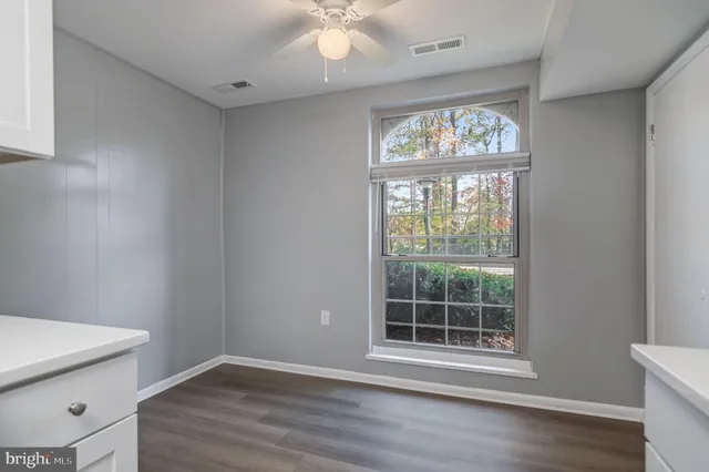 an empty room with wooden floor fan and windows