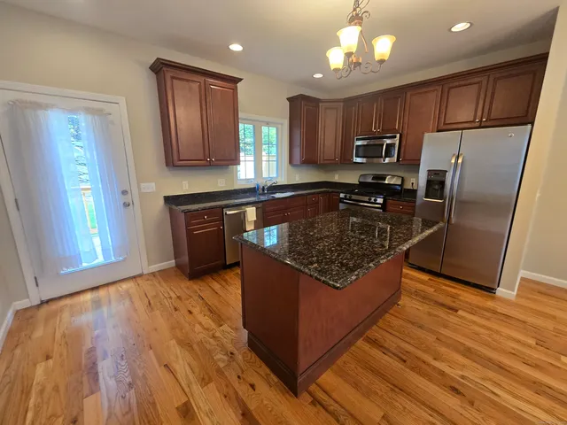 a kitchen with stainless steel appliances granite countertop a stove a refrigerator and a sink with wooden floors