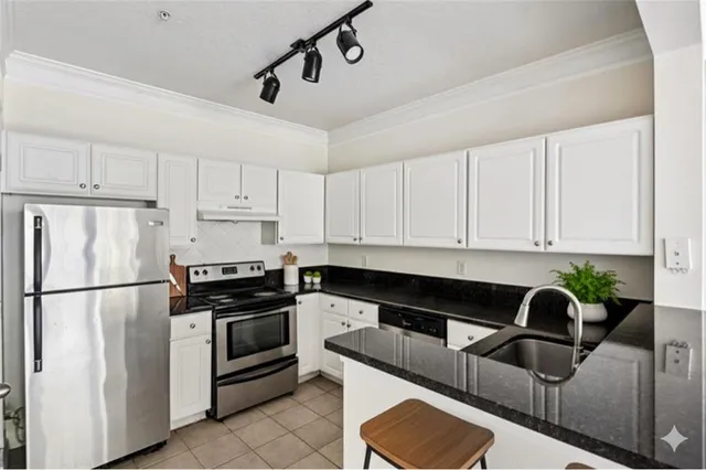 a view of kitchen with stainless steel appliances granite countertop a refrigerator a stove a sink and white cabinets