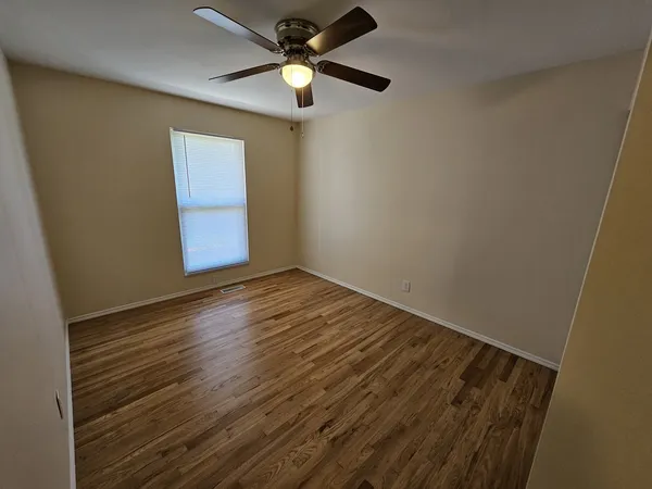 a view of an empty room with wooden floor and a window