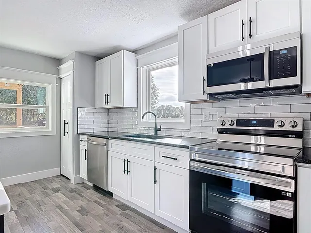 a kitchen with granite countertop a wooden floor a center island cabinets and stainless steel appliances