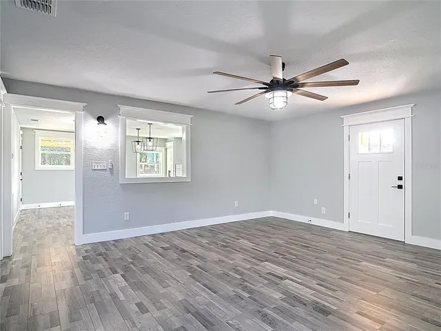 a view of an empty room with wooden floor and a ceiling fan