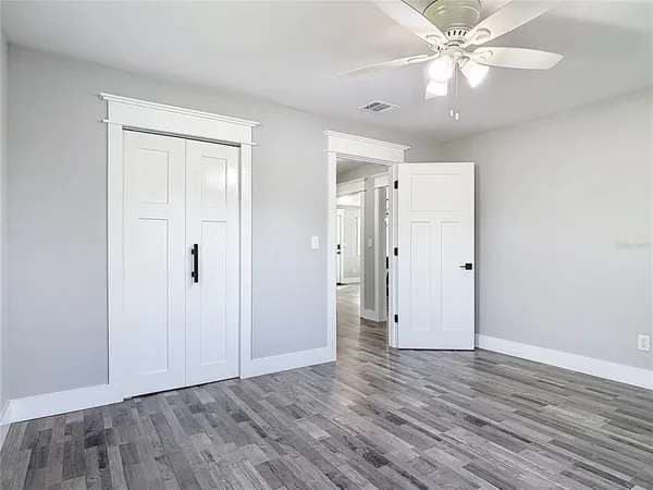 an empty room with wooden floor chandelier fan and windows