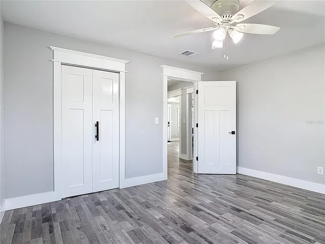 an empty room with wooden floor chandelier fan and windows