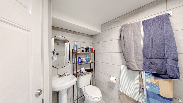 630 1100 West Provo, UT 84601 - Photo 29 of 64 Bathroom featuring a pedestal sink with a chrome faucet, oval mirror, and tiled walls extending to the ceiling