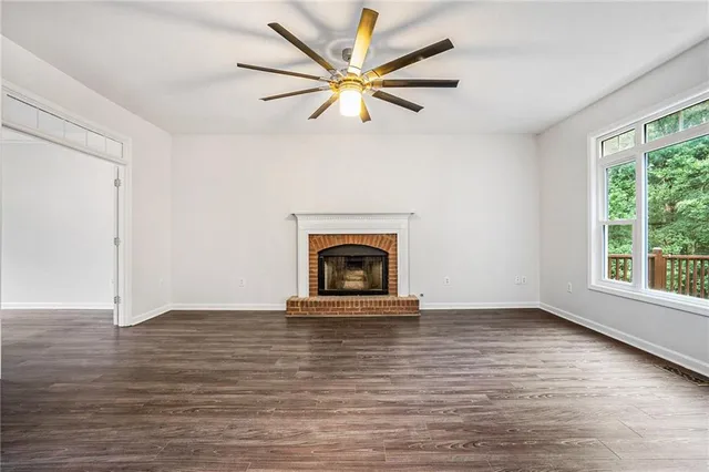 an empty room with windows a fireplace a ceiling fan and wooden floor