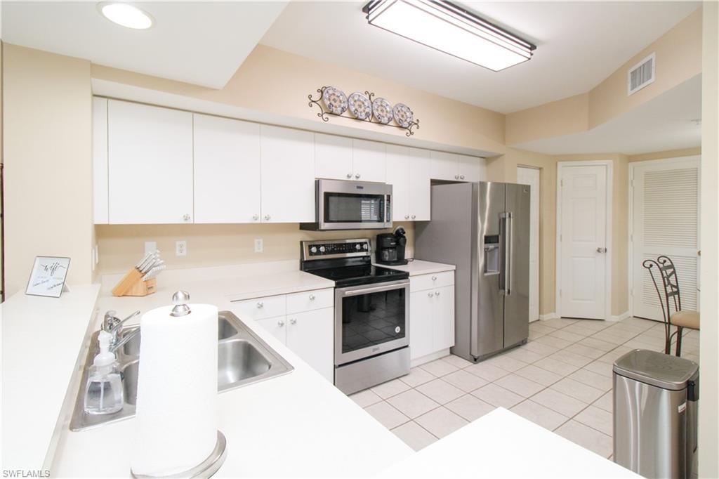 5025 Cedar Springs Drive, Unit 102 Naples, FL 34110 - Photo 22 of 50 Kitchen featuring light tile patterned flooring, appliances with stainless steel finishes, and white cabinets