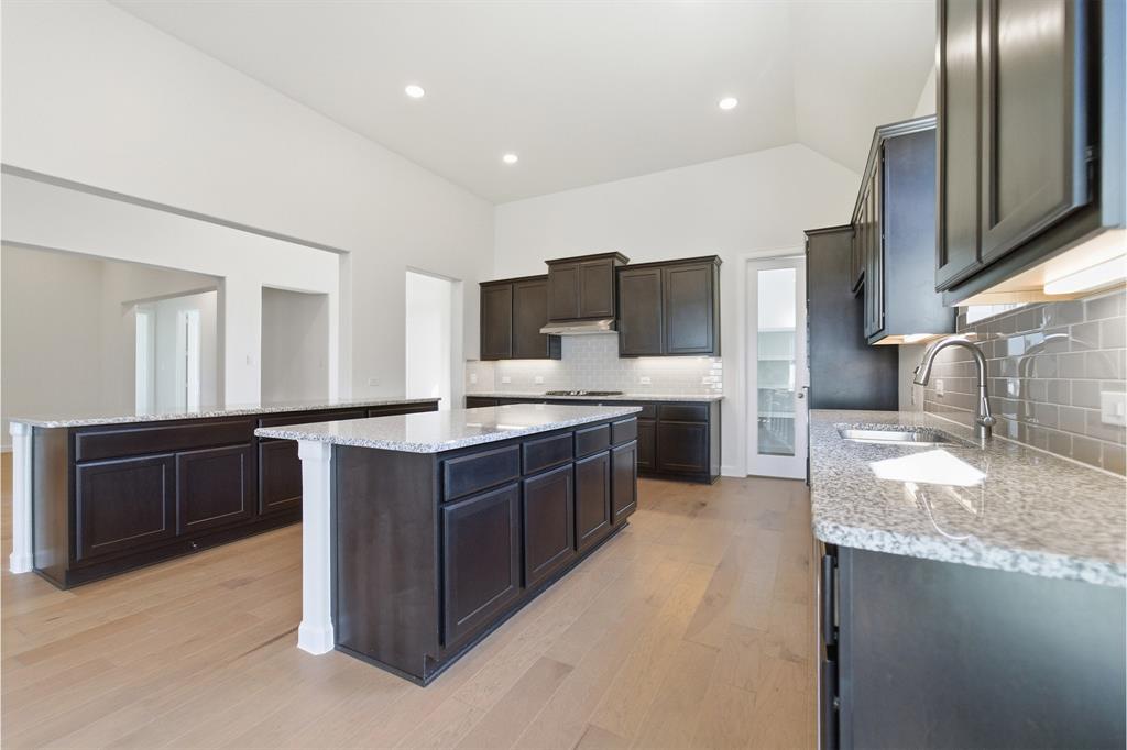 2020 Casting Ridge Mesquite, TX 75181 - Photo 10 of 34 Open-concept kitchen featuring dark wood cabinetry, light granite countertops, a subway tile backsplash, a stainless steel sink with a gooseneck faucet, and light wood-finish flooring