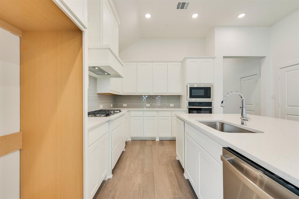 528 Embargo Drive Fate, TX 75189 - Photo 16 of 36 a kitchen with a sink dishwasher stove and white cabinets with wooden floor