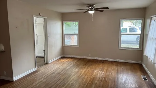 an empty room with wooden floor chandelier fan and windows