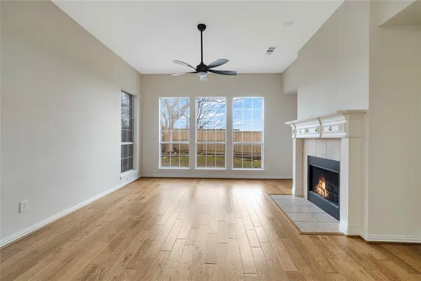 a view of an empty room with wooden floor fireplace and a window