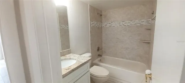 a bathroom with a granite countertop bathtub shower sink vanity and toilet