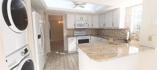 a kitchen with stainless steel appliances granite countertop a refrigerator a sink a stove and white cabinets with wooden floor