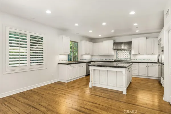 a kitchen with granite countertop a stove a sink and white cabinets with wooden floor