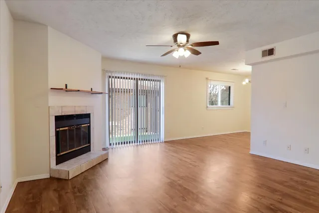 a view of an empty room with wooden floor fireplace and a window