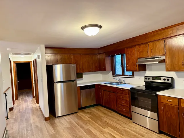 a kitchen with stainless steel appliances granite countertop a refrigerator a sink dishwasher a stove and white countertops with wooden floor