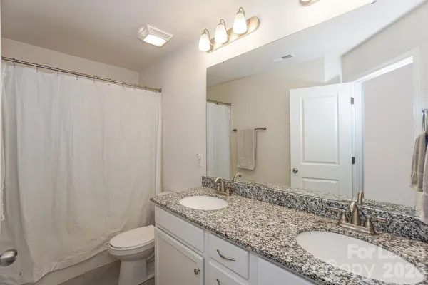 a bathroom with a granite countertop sink a toilet a mirror a vanity and shower