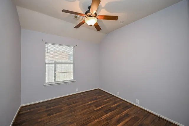an empty room with wooden floor fan and windows