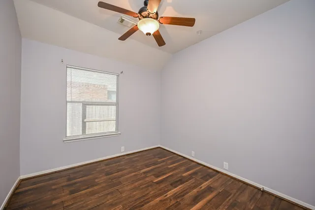 an empty room with wooden floor fan and windows