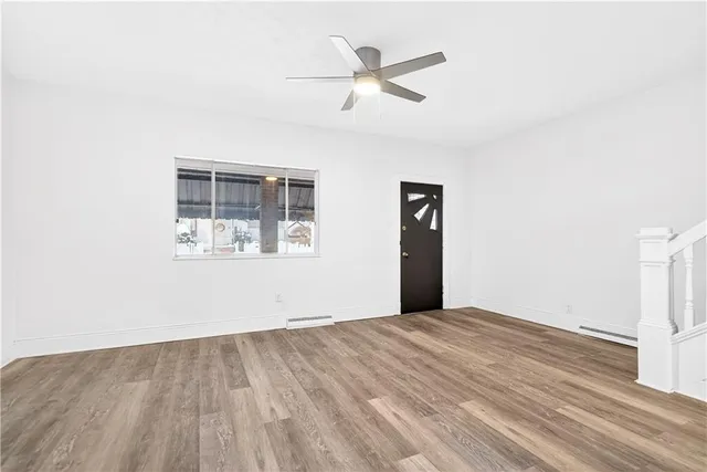 an empty room with wooden floor ceiling fan and windows