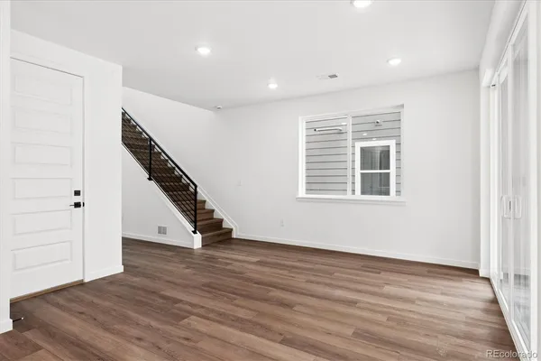 an empty room with wooden floor staircase and windows