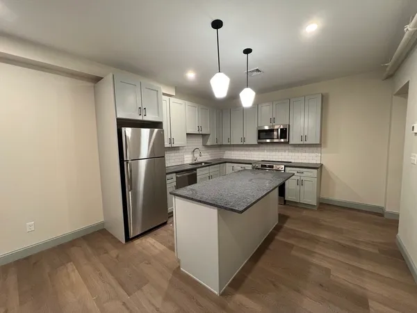 a kitchen with stainless steel appliances granite countertop a sink a stove a refrigerator and island with wooden floor