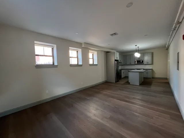 an empty room with wooden floor kitchen view and a kitchen