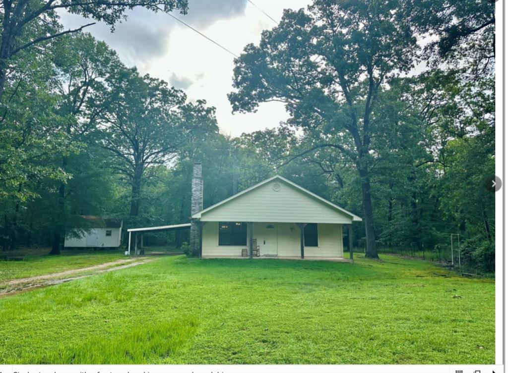 View of front of house with a front yard, a chimney, an attached carport, and view of wooded area