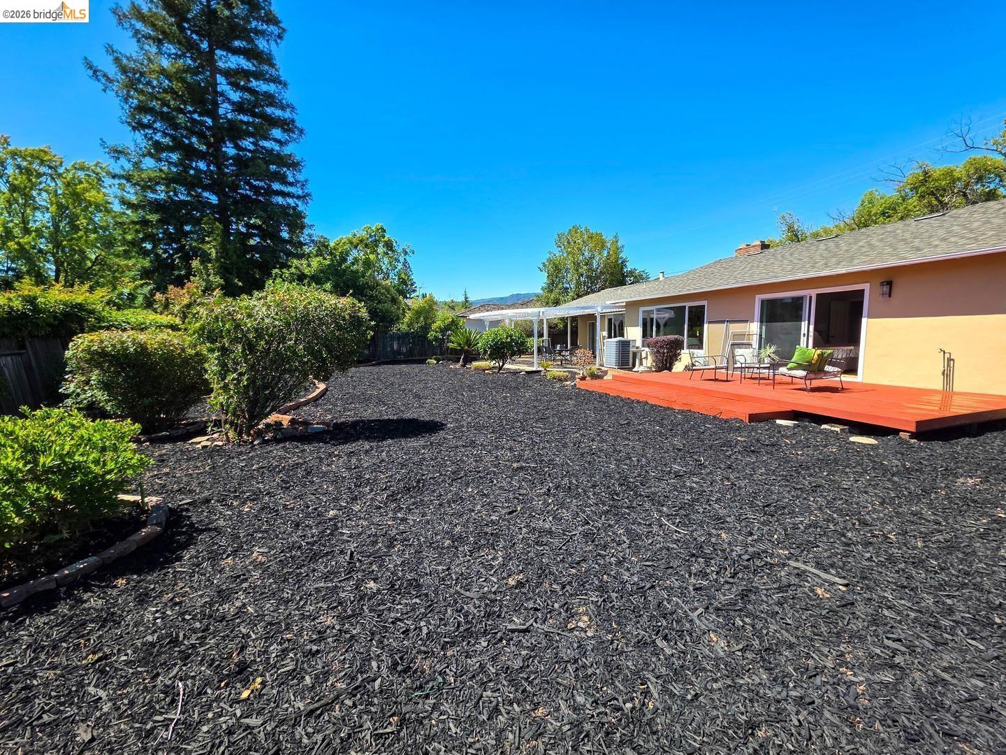 965 Springer Road Los Altos, CA 94024 - Photo 3 of 31 Expansive backyard featuring a vibrant red deck, black wood chip ground cover, and established perimeter landscaping