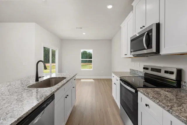 a kitchen with granite countertop a sink a stove top oven a counter space and cabinets