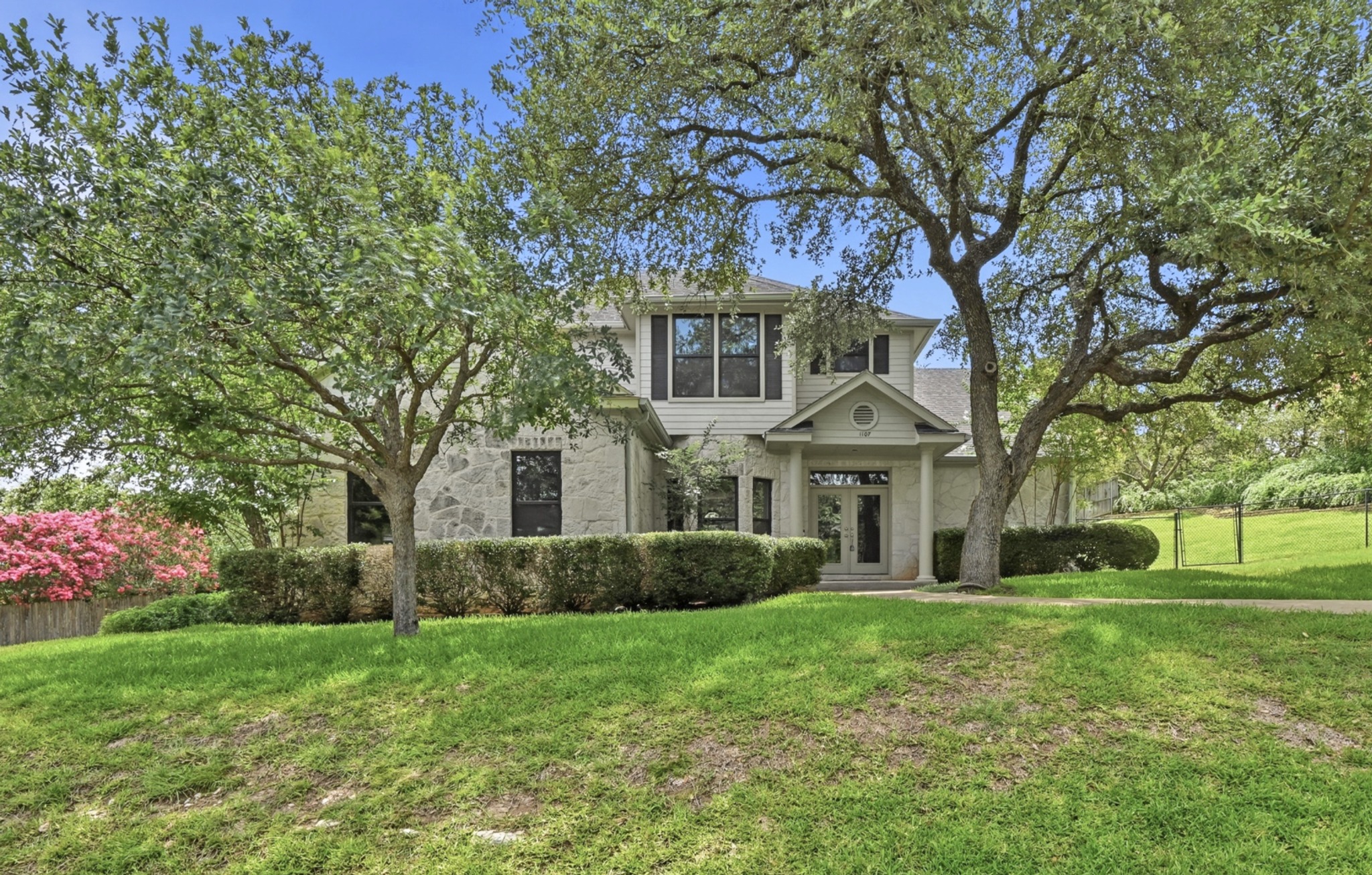 1107 Bowie Road Austin, TX 78733 - Photo 3 of 40 A classic facade with a covered entry and stone accents framed by mature trees and lush landscaping.