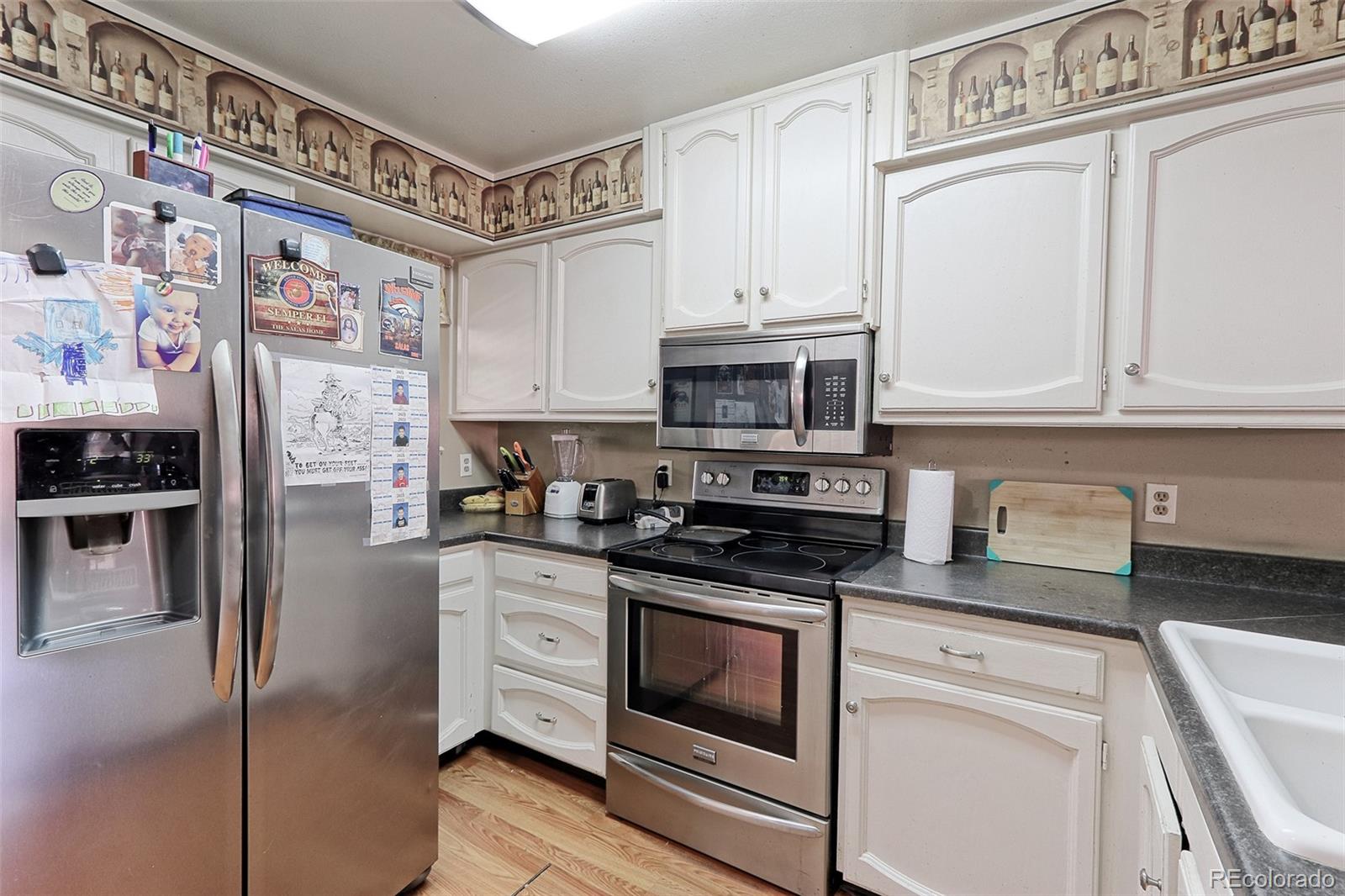 12133 Bannock Circle, Unit B Westminster, CO 80234 - Photo 4 of 14 a kitchen with stainless steel appliances granite countertop a refrigerator a stove and white cabinets with wooden floor